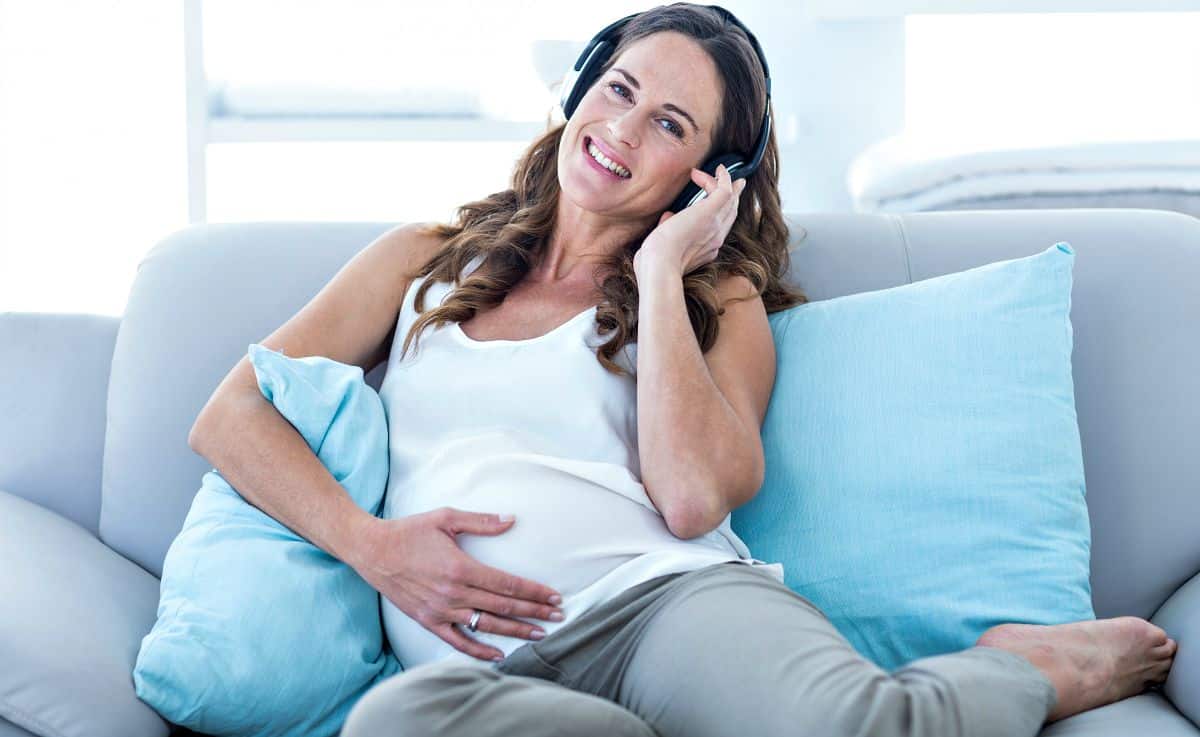A pregnant woman listening to music on sofa at home | What You Need to Pack To Prepare For Baby's Arrival