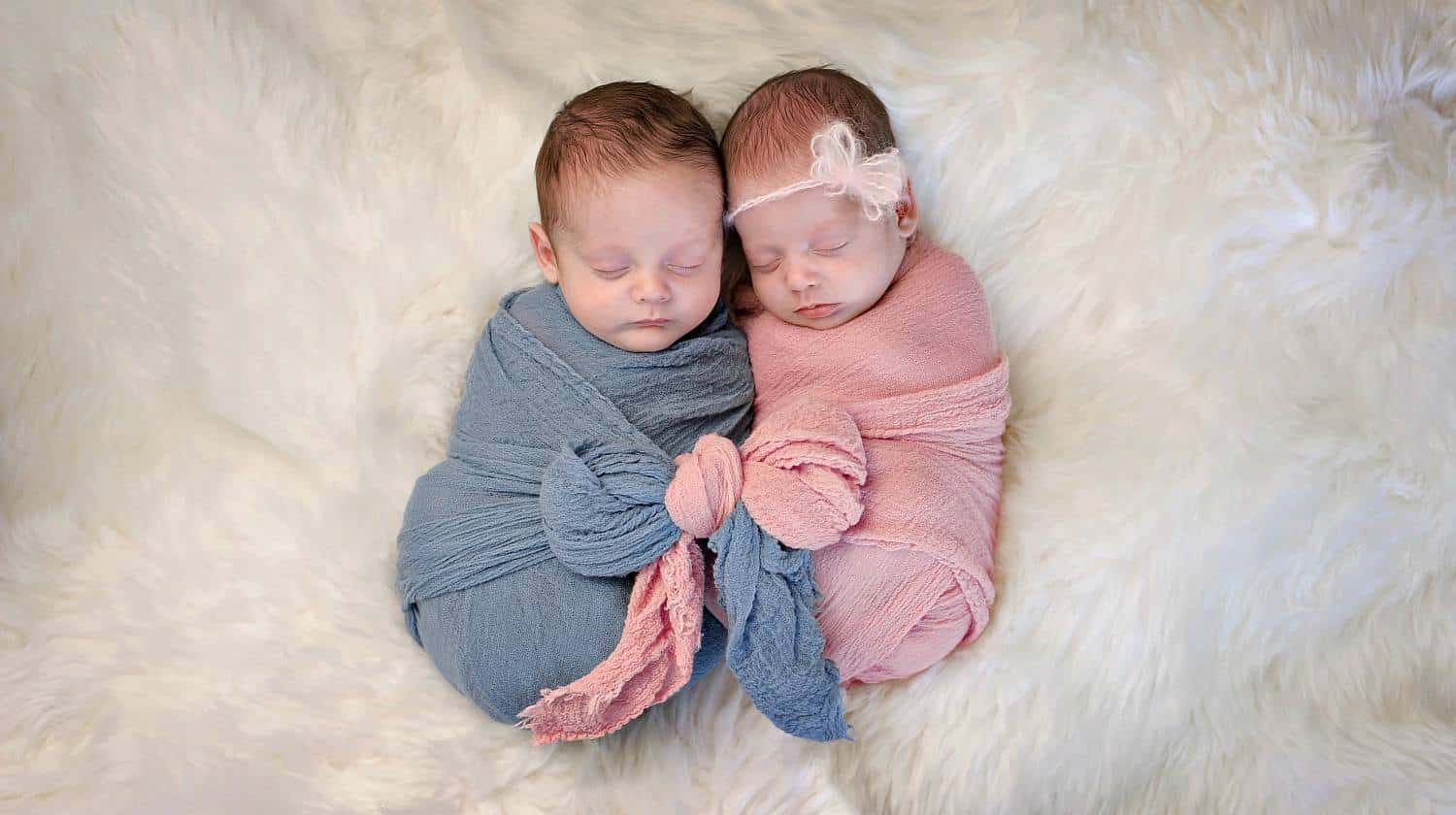 Feature | Sleeping boy and girl fraternal twin swaddled together in pink and blue wraps that are tied together in a bow | Do's and Dont's For Swaddling Your Newborn Baby